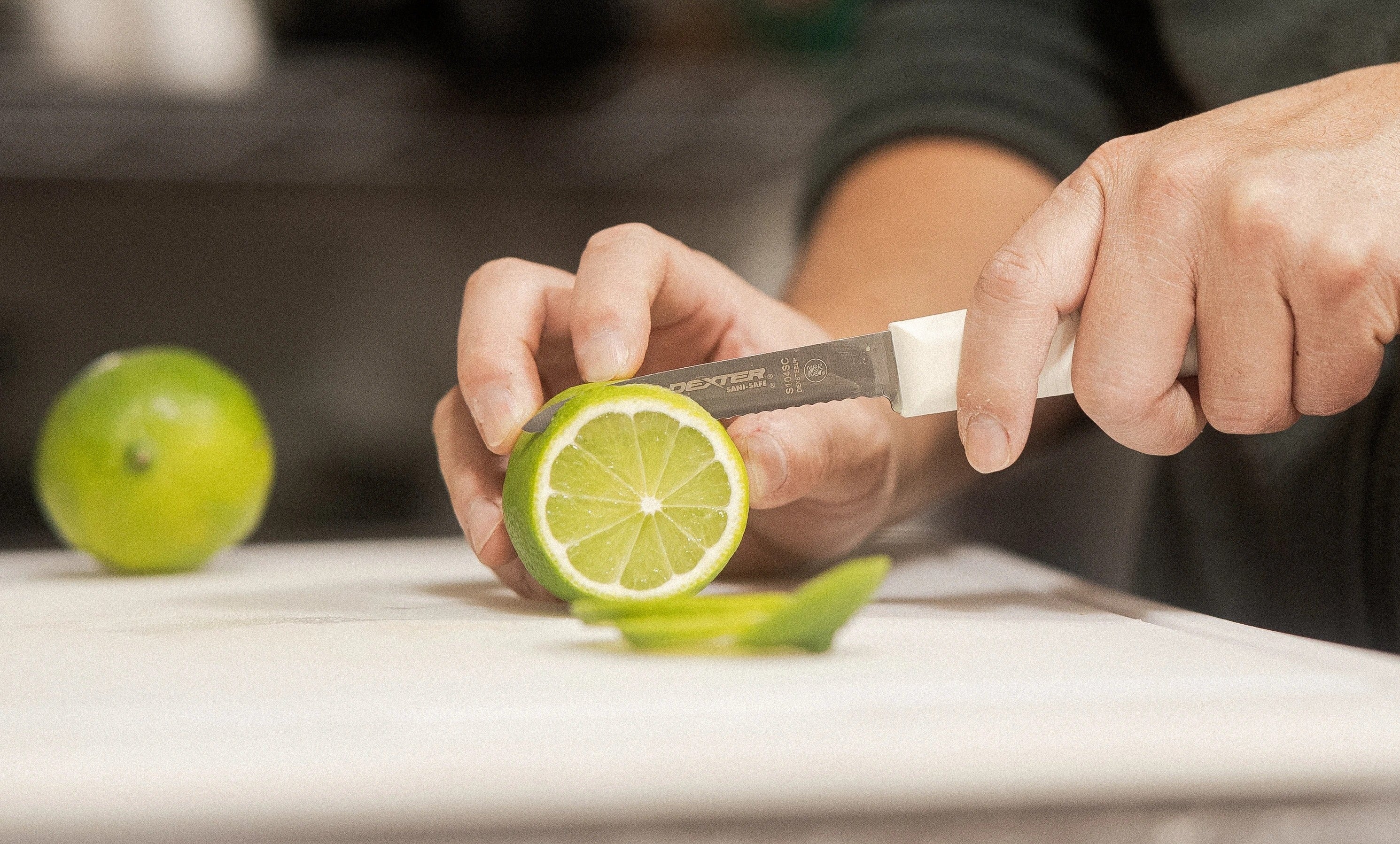 Person cutting a lime with a knife on a cutting board